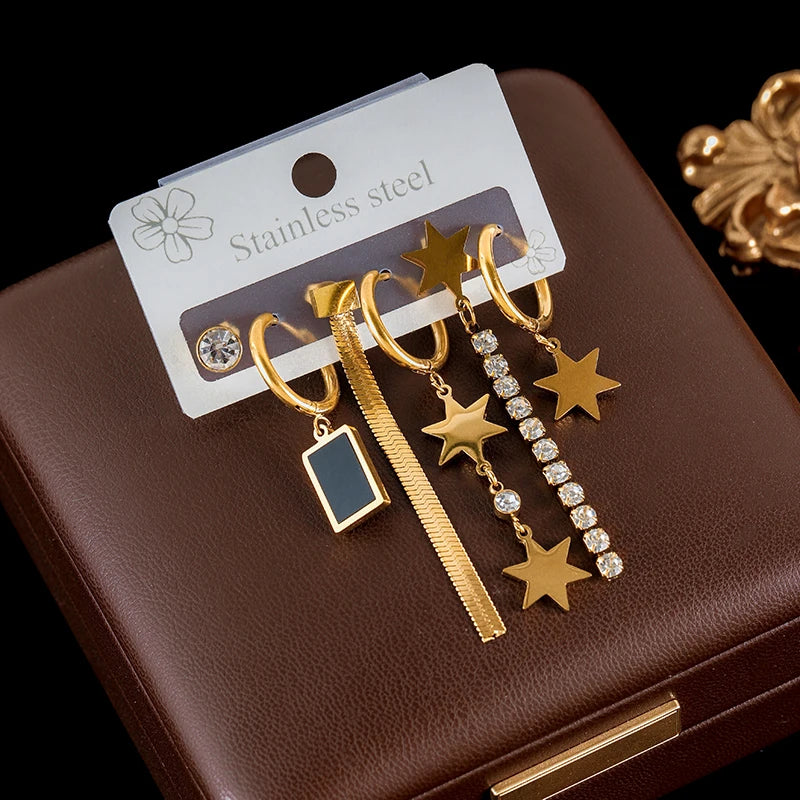 Gold earrings with star and rectangular designs on a brown jewelry box