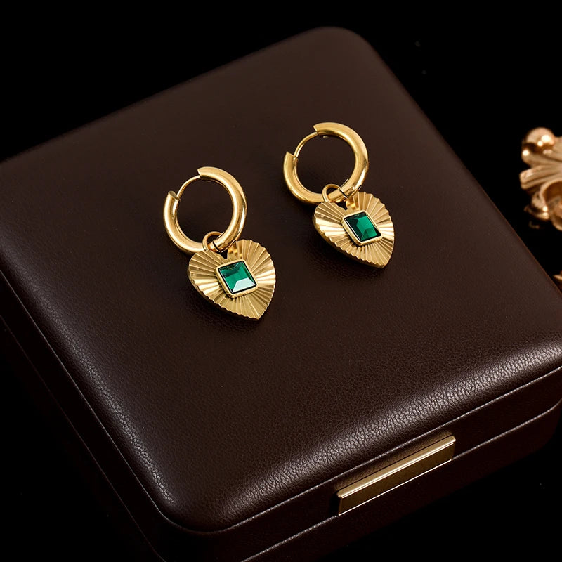 Gold hoop earrings with green gemstones on a brown jewelry box