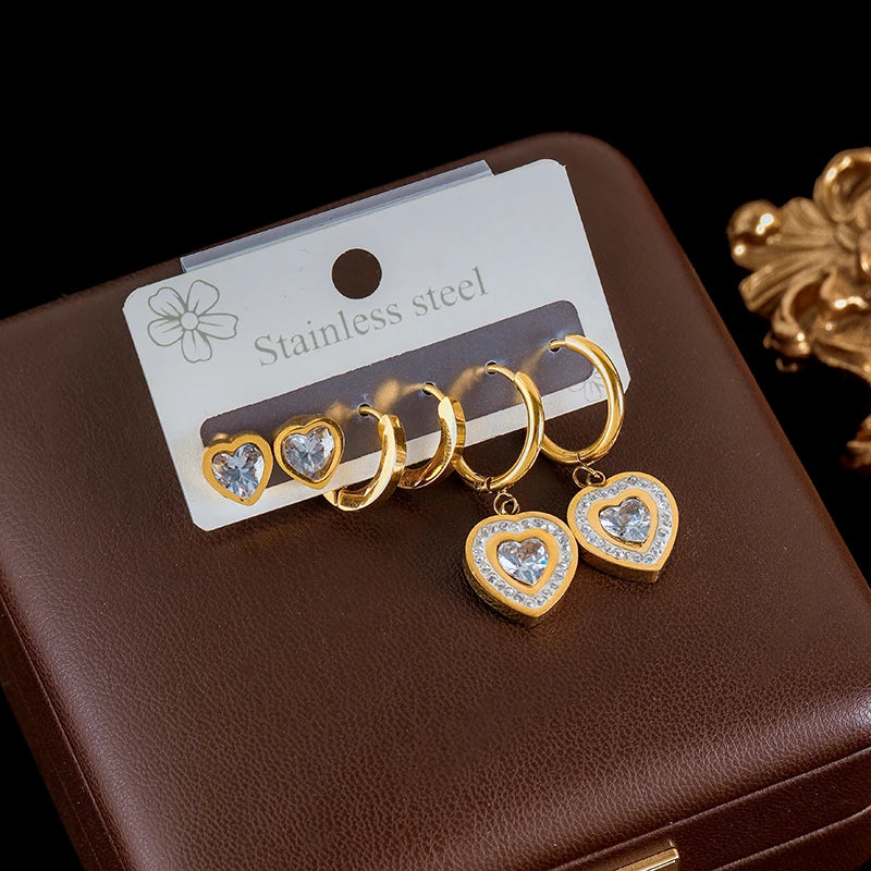 Gold heart-shaped earrings with clear stones on a brown jewelry box