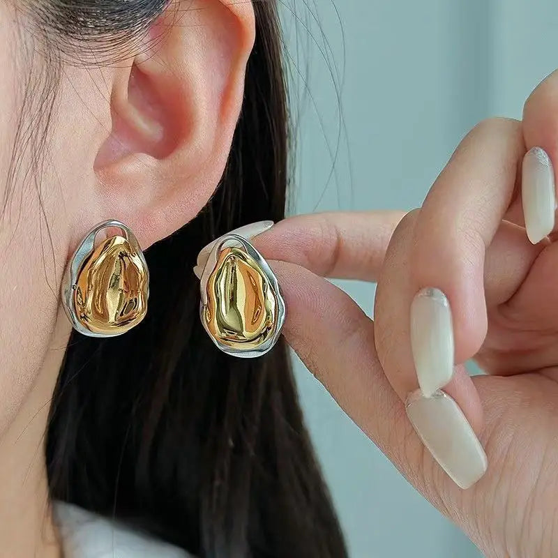 Gold earrings being worn and held by a person against a light blue background