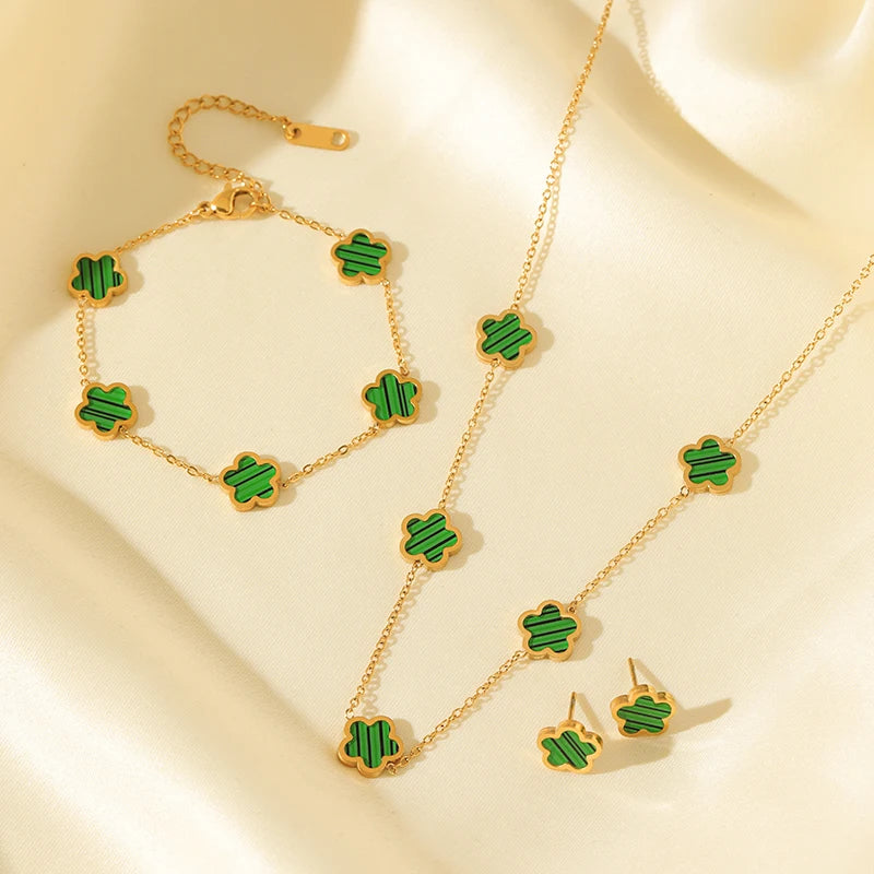 Gold jewelry set with green clover-shaped stones on a beige background