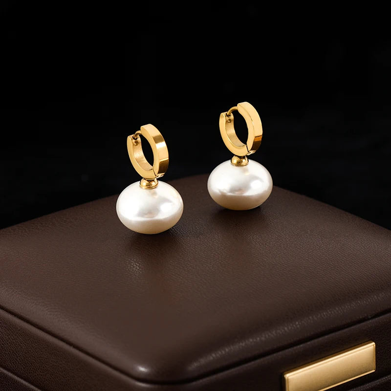 Gold hoop earrings with white pearls on a dark surface