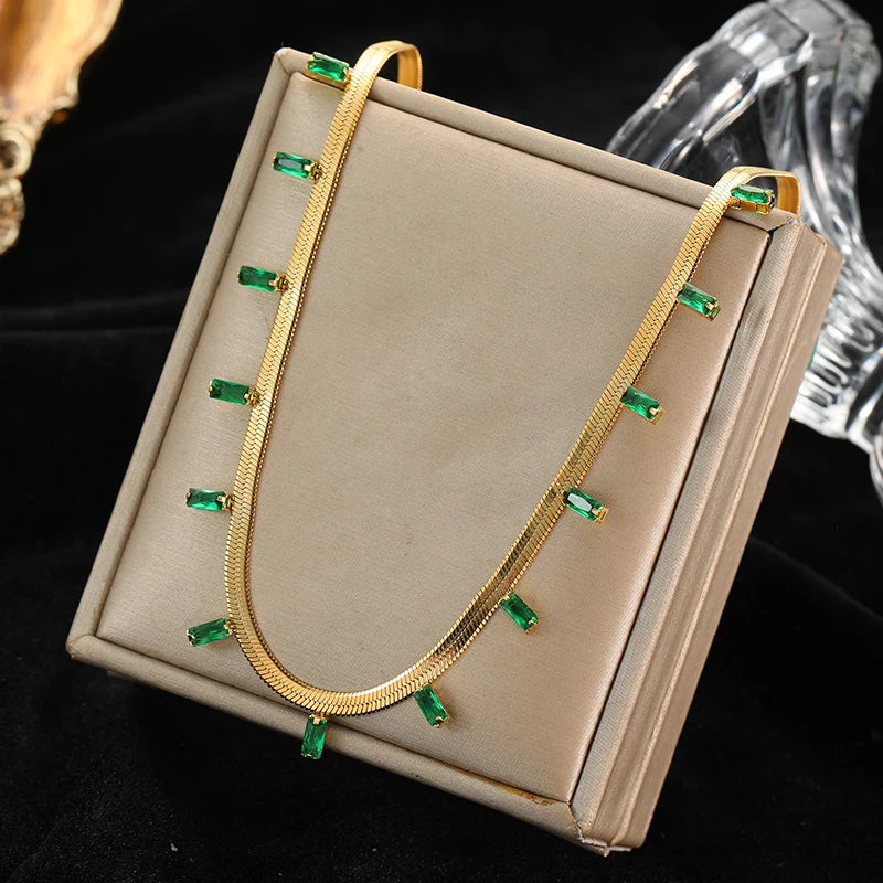 Gold necklace with green gemstones on a beige display box against a black background