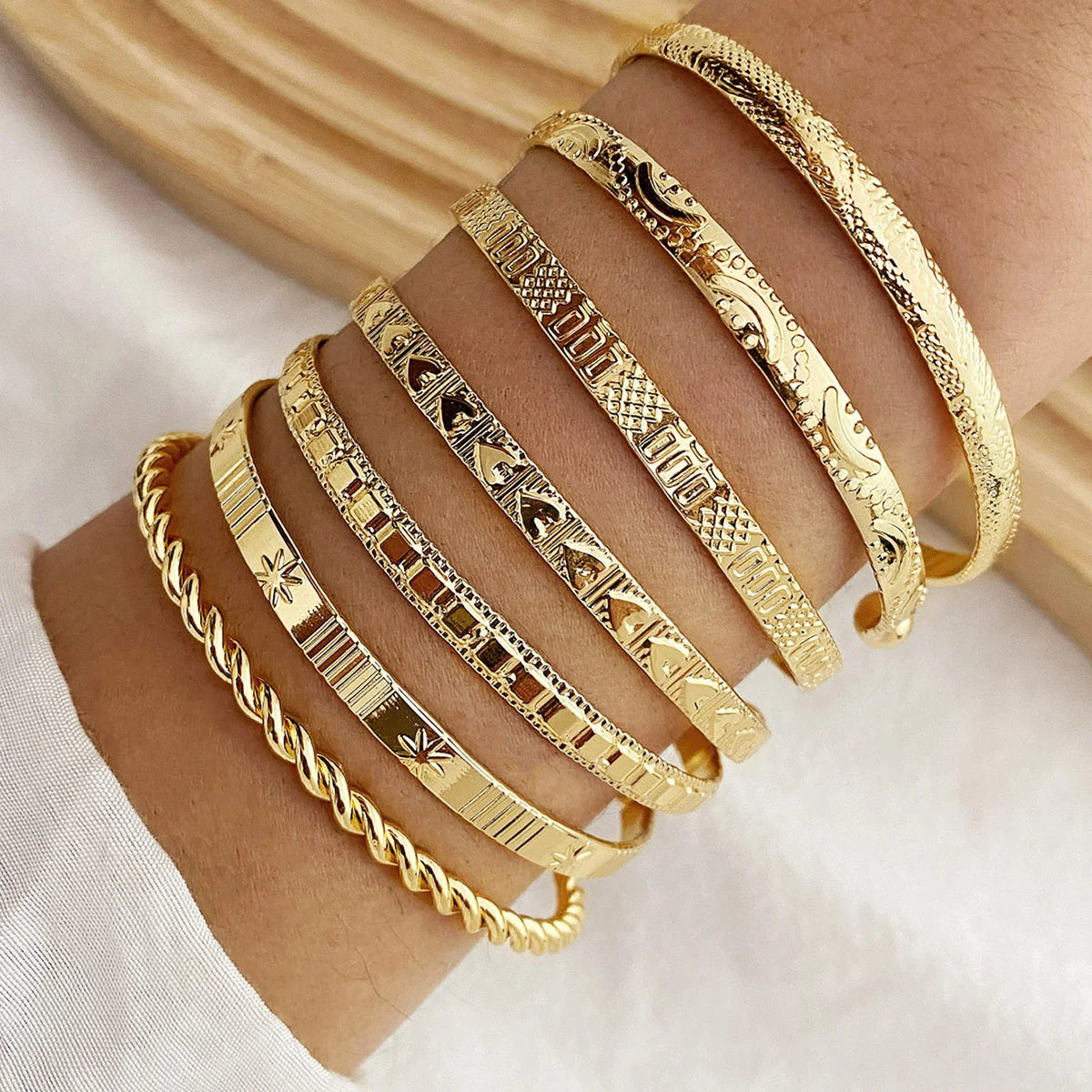 Gold bracelets with various patterns on a wrist against a neutral background