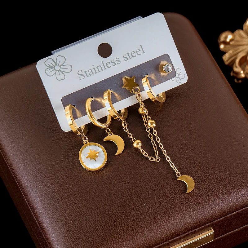 Gold earrings with star, moon, and sun designs on a brown surface with a 'Stainless steel' label.