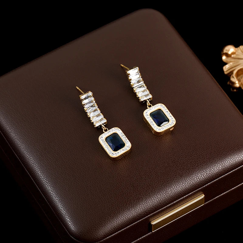 Pair of gold earrings with blue gemstones on a brown jewelry box.